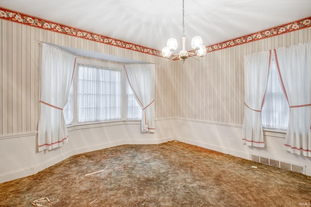 carpeted empty room featuring an inviting chandelier