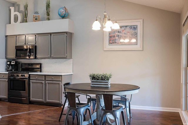 kitchen featuring gray cabinetry, backsplash, lofted ceiling, decorative light fixtures, and appliances with stainless steel finishes