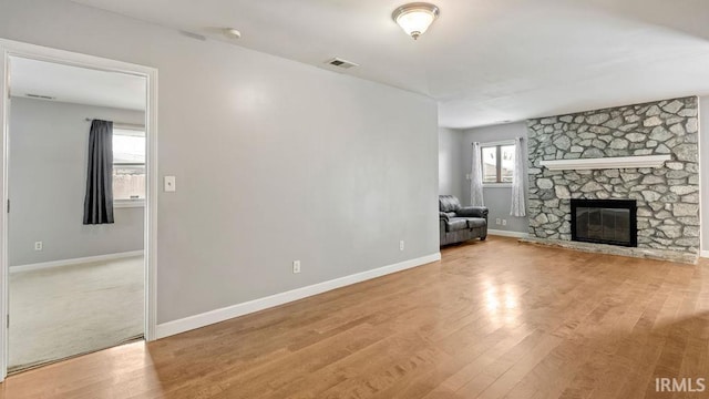 unfurnished living room featuring light wood-type flooring and a stone fireplace