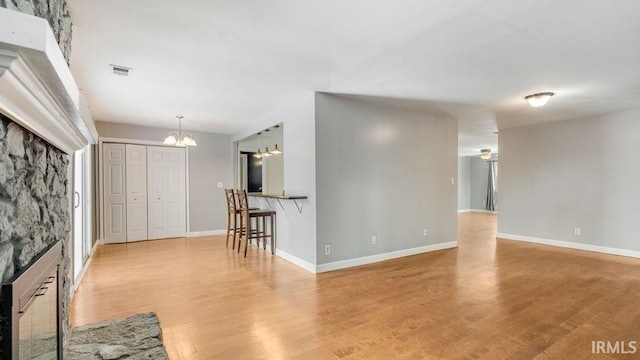 unfurnished living room with a stone fireplace, light hardwood / wood-style flooring, and a chandelier