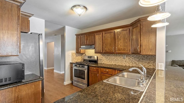 kitchen with decorative backsplash, light wood-type flooring, stainless steel gas range, sink, and decorative light fixtures