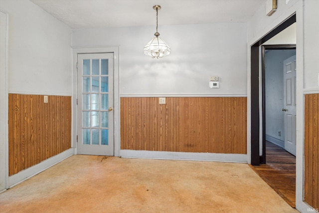 carpeted spare room featuring an inviting chandelier and wood walls