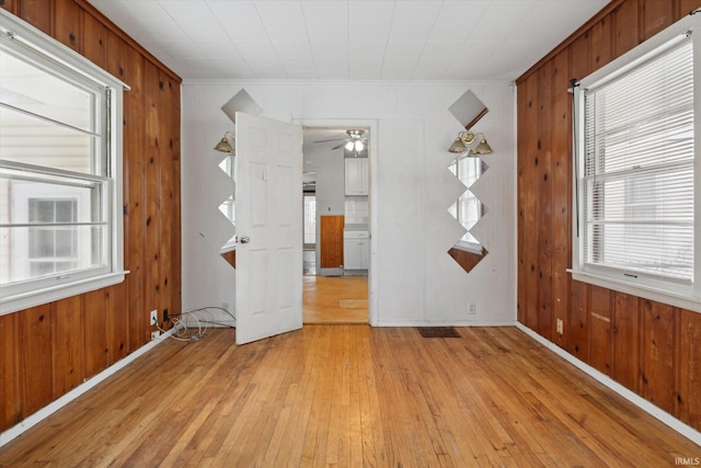 unfurnished room featuring ceiling fan, light wood-type flooring, and wooden walls