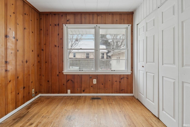 empty room with wood walls and light hardwood / wood-style flooring