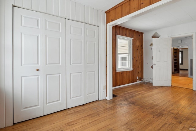 unfurnished bedroom featuring light hardwood / wood-style flooring, wooden walls, and a closet