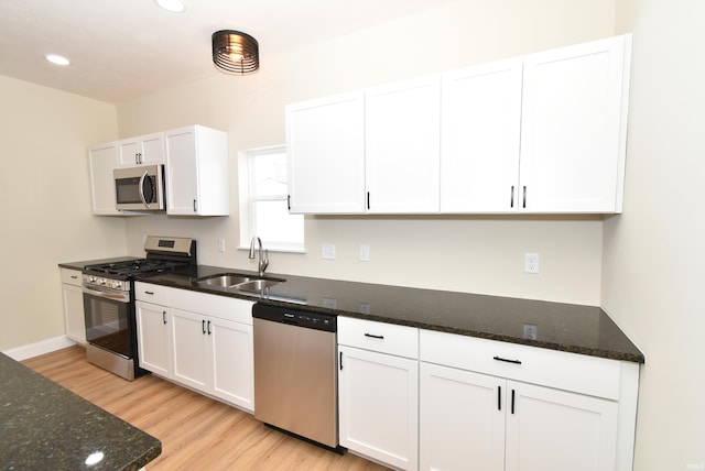 kitchen featuring appliances with stainless steel finishes, white cabinetry, dark stone countertops, and sink