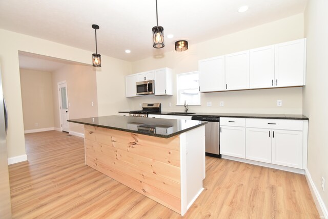 kitchen with pendant lighting, sink, appliances with stainless steel finishes, a kitchen island, and white cabinetry