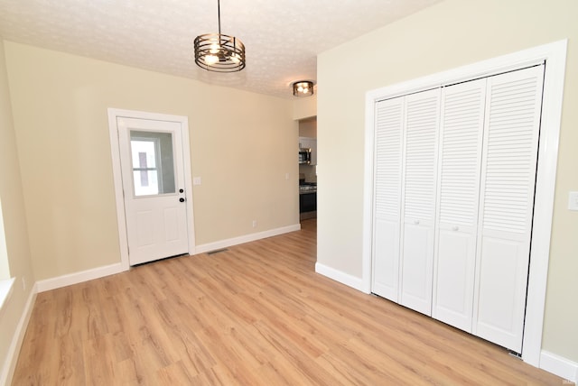 foyer entrance featuring light hardwood / wood-style flooring, a textured ceiling, and an inviting chandelier