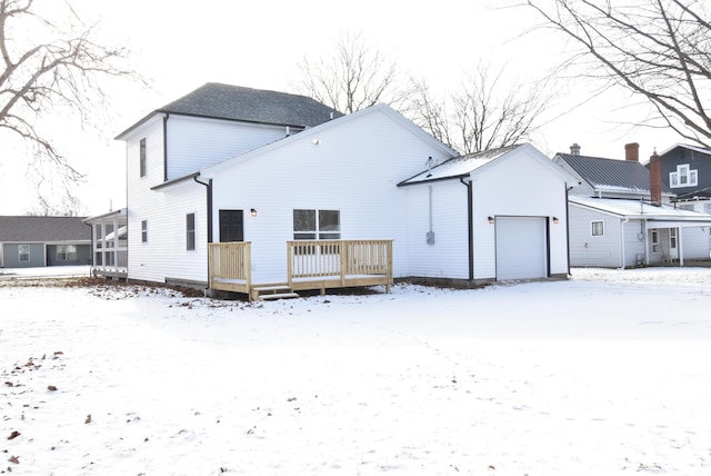 snow covered rear of property featuring a garage and a deck