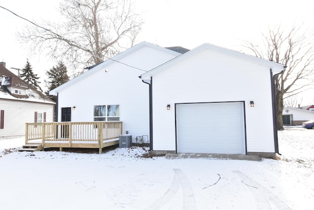 snow covered rear of property featuring a garage, central AC unit, and a wooden deck