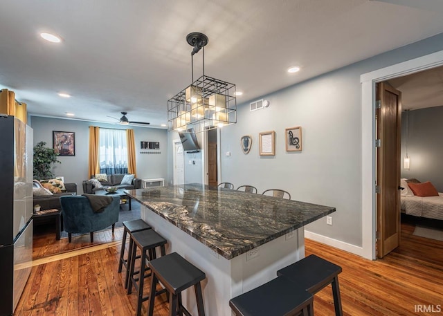 kitchen featuring stainless steel refrigerator, ceiling fan, a kitchen breakfast bar, pendant lighting, and hardwood / wood-style flooring