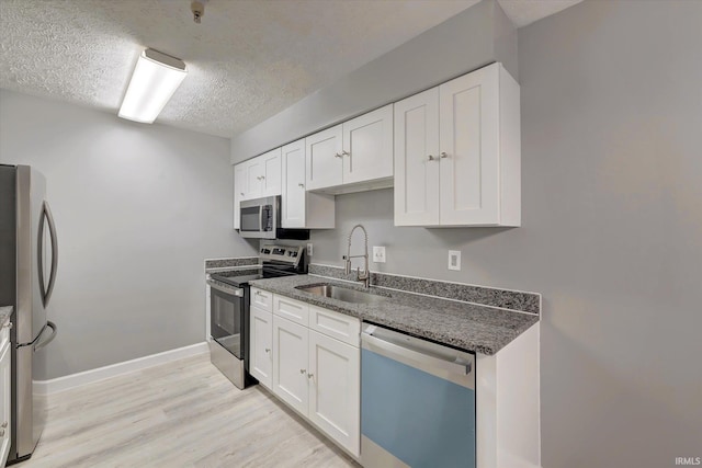 kitchen with appliances with stainless steel finishes, a textured ceiling, sink, light hardwood / wood-style flooring, and white cabinets