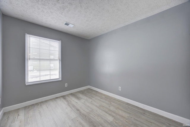 empty room with a textured ceiling and light hardwood / wood-style flooring