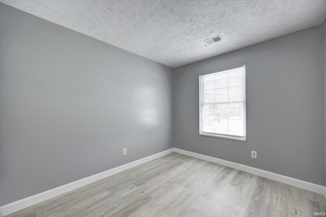 empty room with a textured ceiling and light hardwood / wood-style flooring