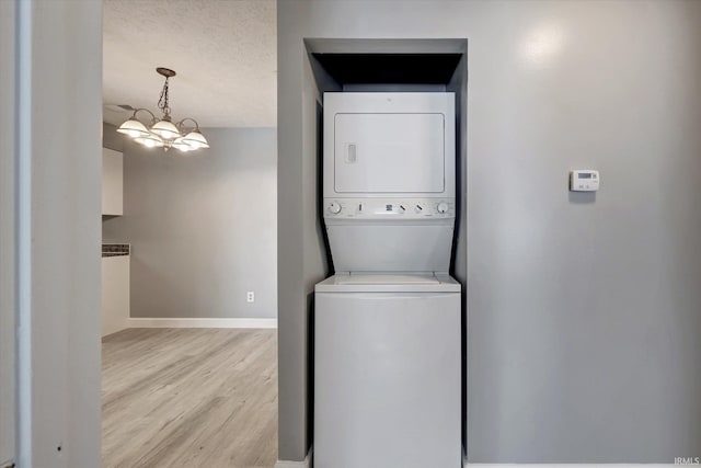 washroom with a textured ceiling, stacked washing maching and dryer, an inviting chandelier, and light hardwood / wood-style floors