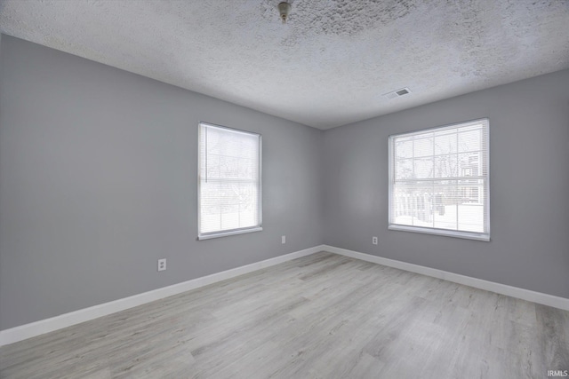 empty room featuring a wealth of natural light, light hardwood / wood-style flooring, and a textured ceiling