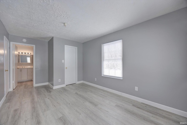 unfurnished bedroom with a textured ceiling, light wood-type flooring, ensuite bathroom, and sink