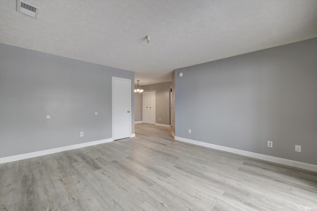 spare room featuring a chandelier, a textured ceiling, and light wood-type flooring