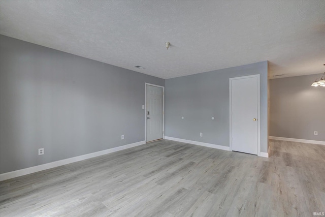 spare room with light wood-type flooring, a textured ceiling, and an inviting chandelier