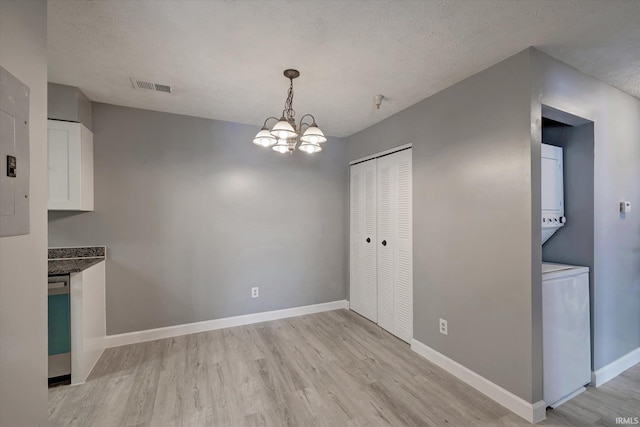 unfurnished dining area featuring light hardwood / wood-style floors, a textured ceiling, and an inviting chandelier