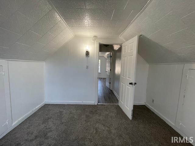 bonus room with dark carpet and vaulted ceiling