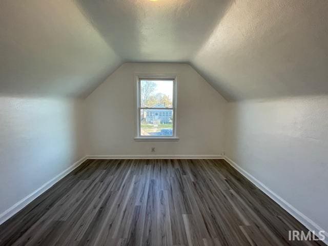 additional living space with a textured ceiling, dark hardwood / wood-style flooring, and lofted ceiling