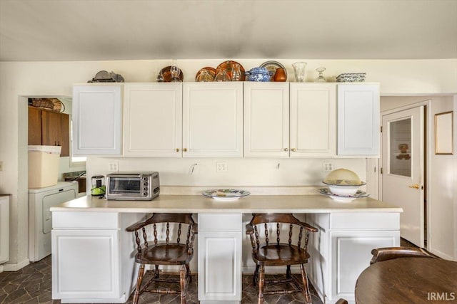 kitchen with white cabinets, a kitchen bar, and washer / clothes dryer