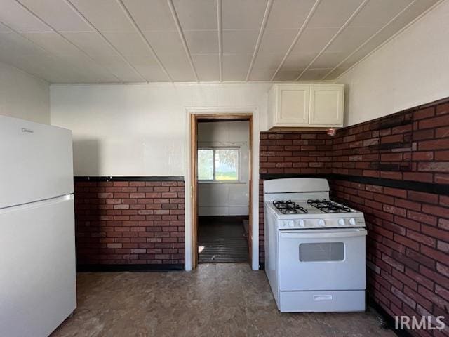 kitchen featuring white cabinets, white appliances, and brick wall