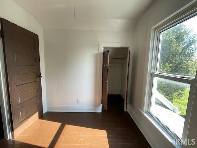 unfurnished bedroom with lofted ceiling, multiple windows, and dark wood-type flooring