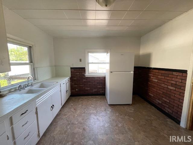 kitchen featuring white cabinetry, sink, white fridge, and brick wall