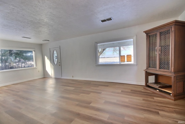 unfurnished living room featuring a textured ceiling, light hardwood / wood-style flooring, and a wealth of natural light