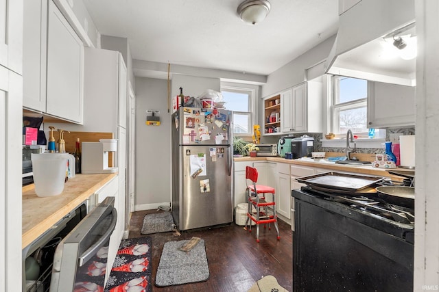 kitchen with black range with electric stovetop, stainless steel fridge, white cabinetry, and a wealth of natural light