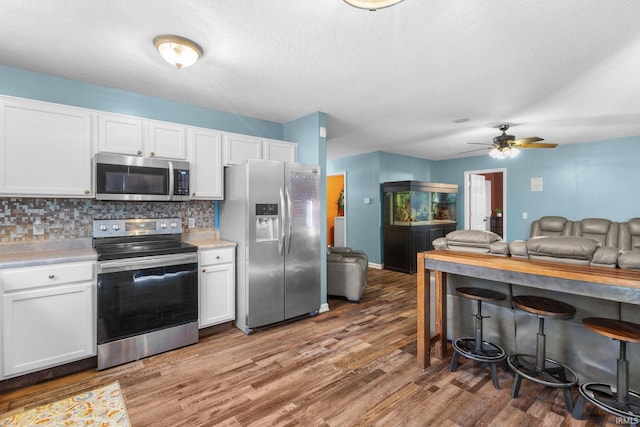 kitchen with backsplash, stainless steel appliances, ceiling fan, wood-type flooring, and white cabinetry