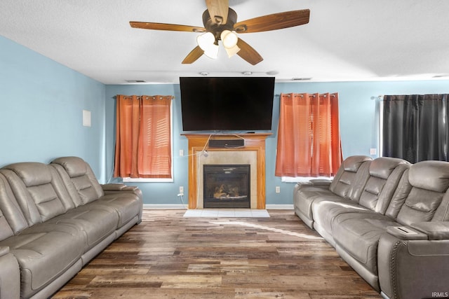 living room with a textured ceiling, dark hardwood / wood-style flooring, ceiling fan, and a tiled fireplace