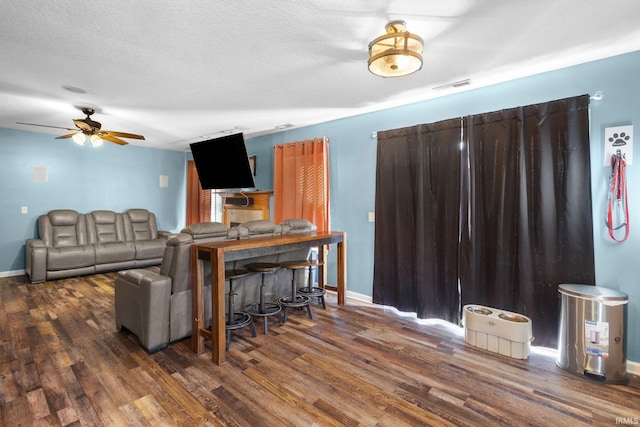 living room with a textured ceiling, ceiling fan, and dark wood-type flooring