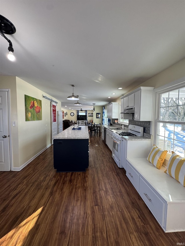 kitchen featuring white appliances, a barn door, a center island, dark hardwood / wood-style floors, and hanging light fixtures