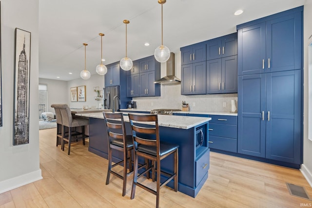 kitchen featuring a center island with sink, hanging light fixtures, wall chimney exhaust hood, and a breakfast bar area