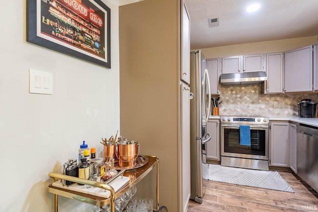 kitchen with backsplash, stainless steel appliances, gray cabinets, and light hardwood / wood-style flooring