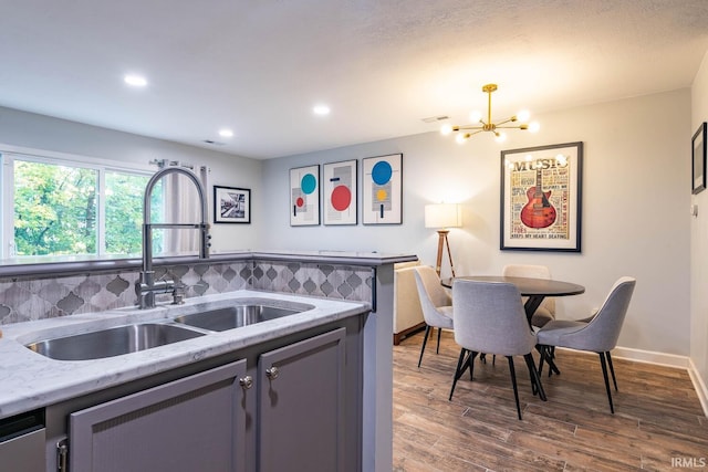 kitchen with tasteful backsplash, light stone counters, dark wood-type flooring, sink, and an inviting chandelier