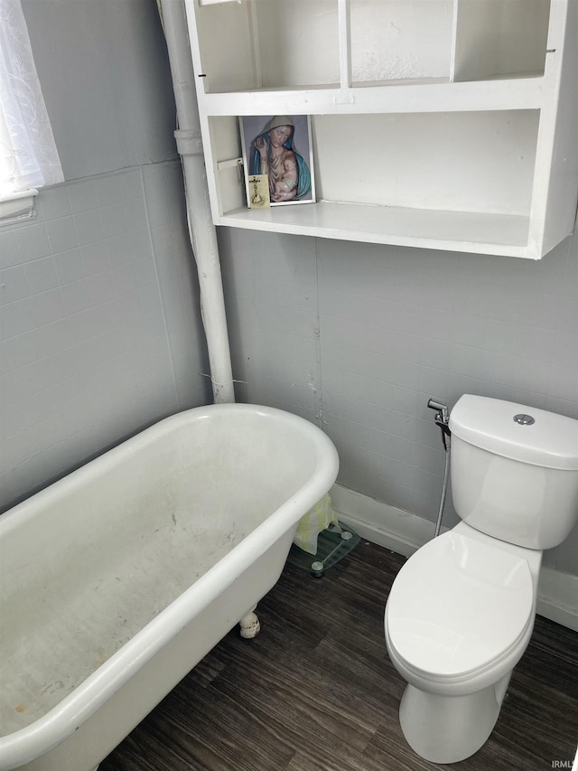 bathroom with a washtub, toilet, and hardwood / wood-style flooring