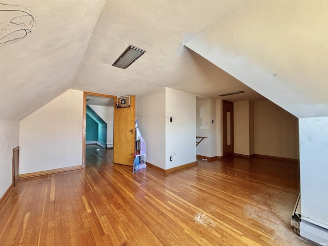 additional living space featuring lofted ceiling, a textured ceiling, and hardwood / wood-style flooring