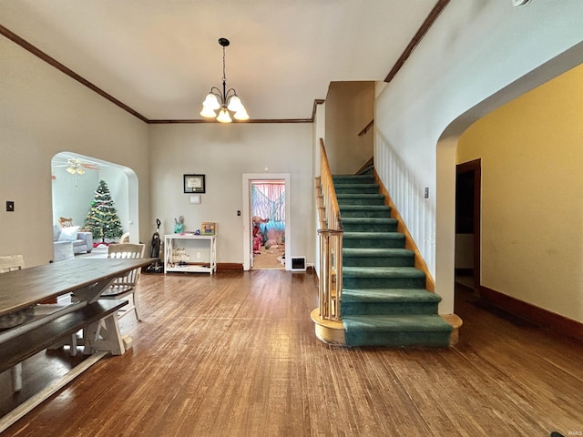 interior space with a towering ceiling, hardwood / wood-style floors, ceiling fan with notable chandelier, and crown molding