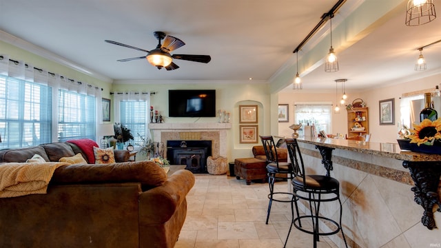 living room with ceiling fan, a healthy amount of sunlight, ornamental molding, and a wood stove