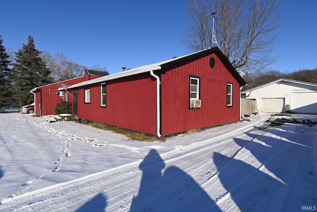 snow covered property featuring cooling unit, a garage, and an outdoor structure