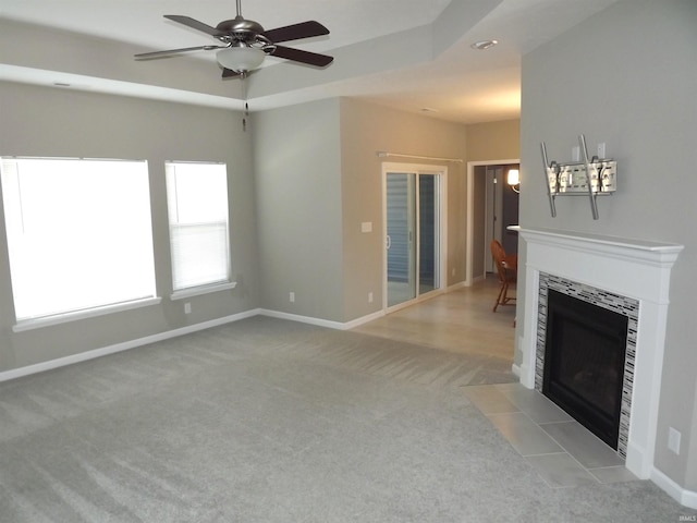 unfurnished living room with a raised ceiling, a tile fireplace, ceiling fan, and light colored carpet