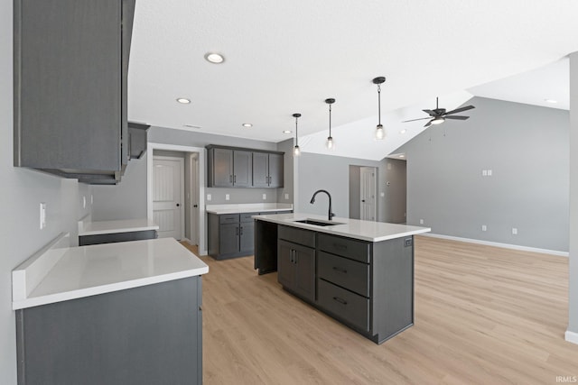 kitchen featuring gray cabinetry, vaulted ceiling, a kitchen island with sink, sink, and decorative light fixtures