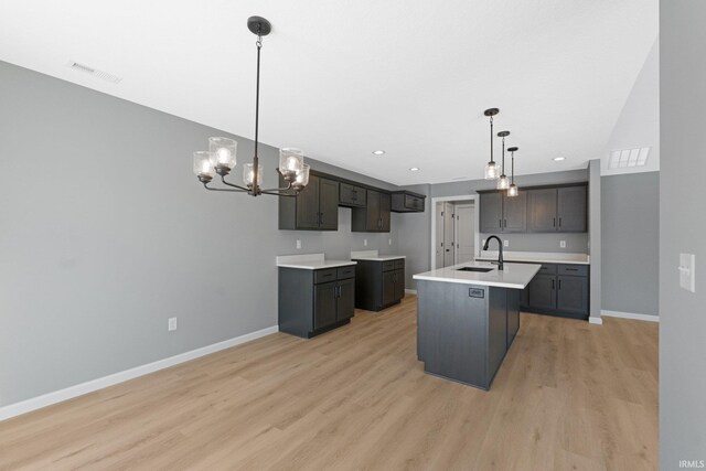 kitchen with sink, an island with sink, hanging light fixtures, and light hardwood / wood-style floors