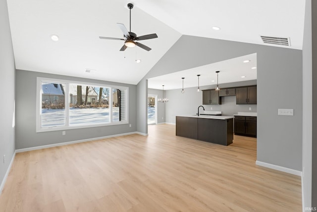 kitchen with an island with sink, light hardwood / wood-style floors, decorative light fixtures, dark brown cabinets, and ceiling fan with notable chandelier