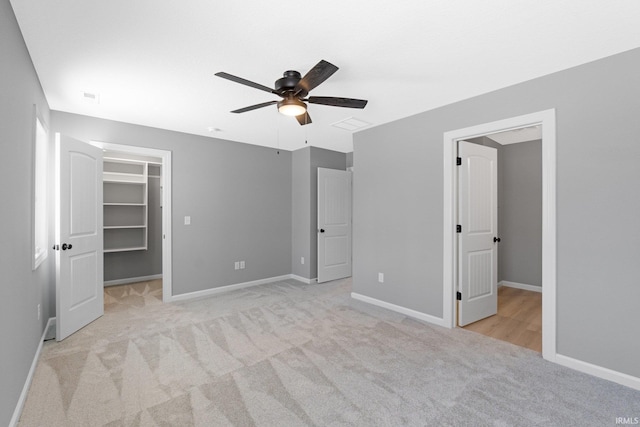 unfurnished bedroom featuring ceiling fan, a spacious closet, light carpet, and a closet