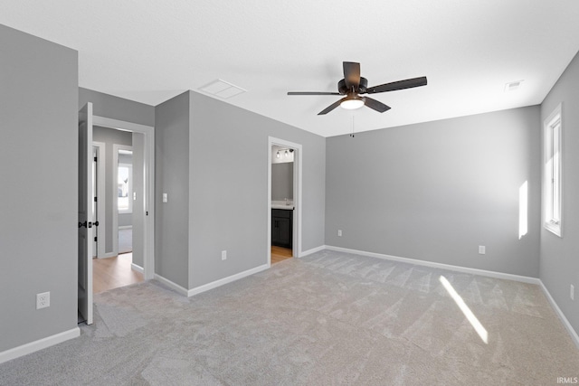 unfurnished bedroom featuring ensuite bath, ceiling fan, light carpet, and multiple windows